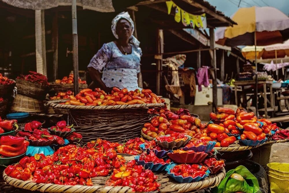 A market vendor stands behind baskets of fresh chili peppers and tomatoes
